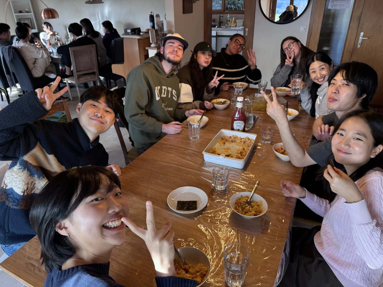 Students and staff around a long dinner table, smiling and waving at the camera