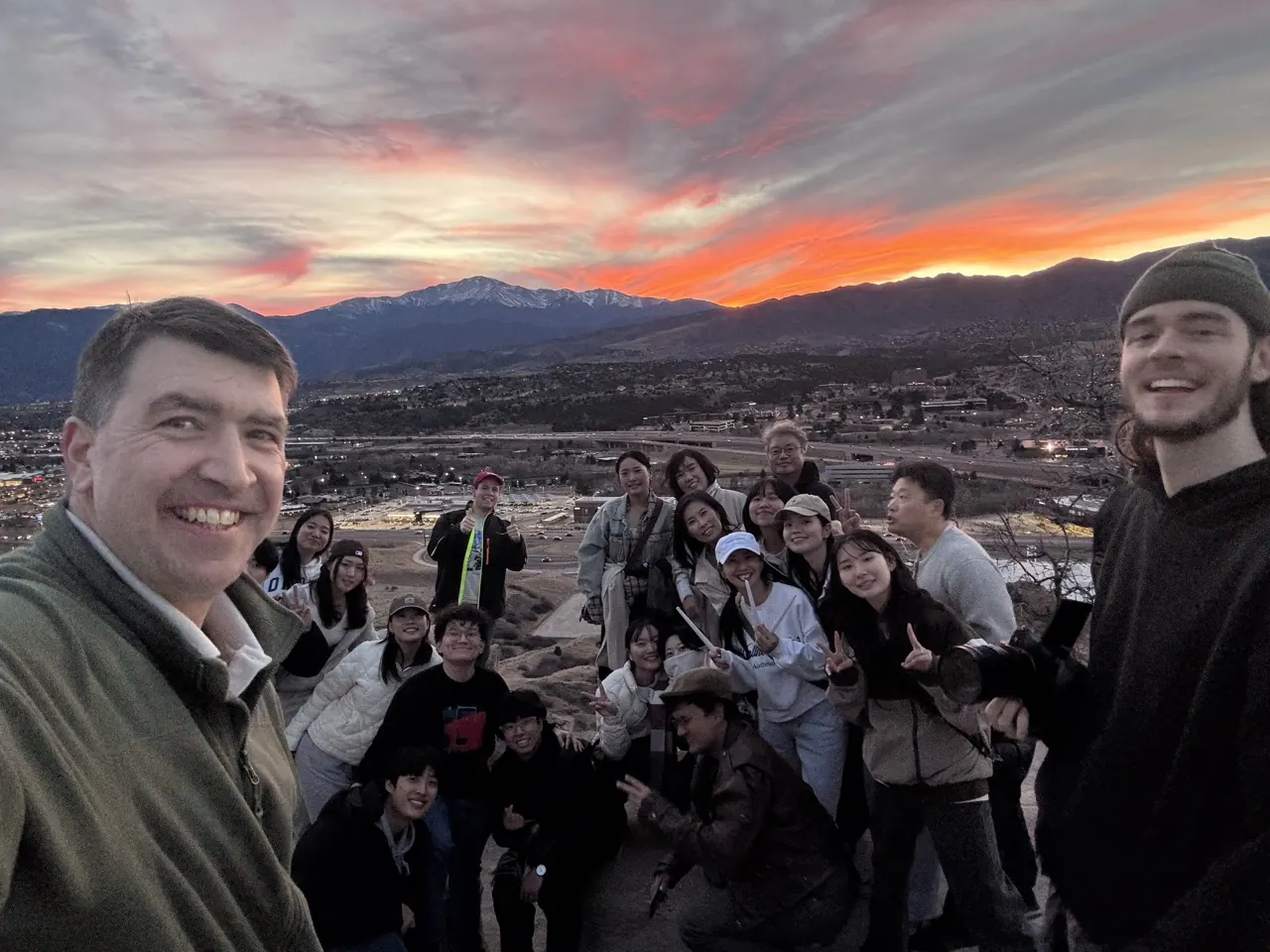 Vince taking a selfie with a group of students on a hilltop at sunset
