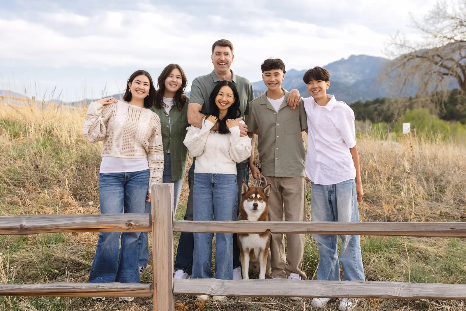The Licari family and their husky by a wooden fence, with the Colorado mountains behind them